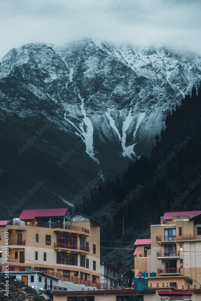 vertical image of hotels with mountains in background and snow on top in naran kaghan valley