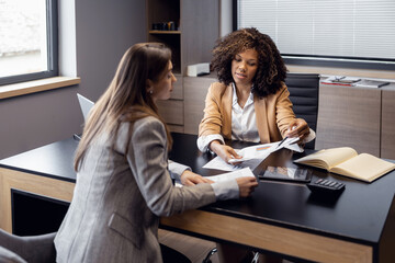 Female travel agent looking at her client, communicating with her in office and showing tours