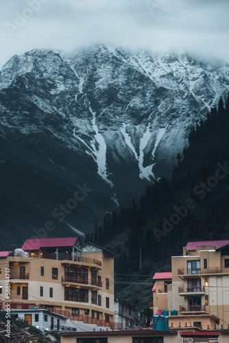 vertical image of hotels with mountains in background and snow on top in naran kaghan valley