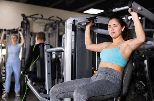 Athletic woman is engaged in the simulator - develops biceps and triceps
