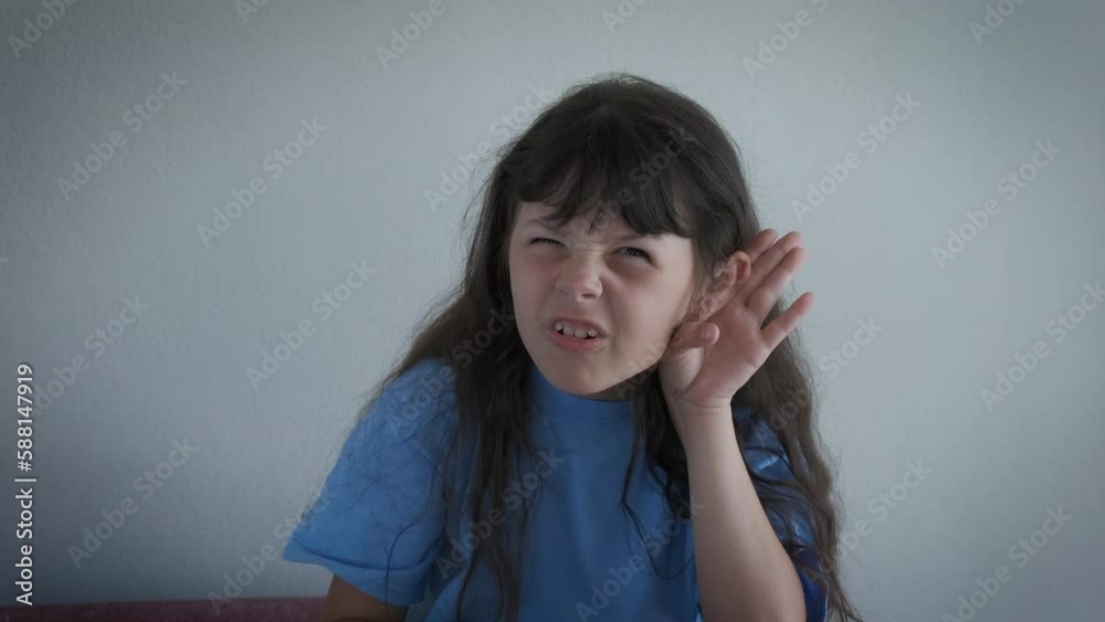 Child with hearing problems indoor. A confused little girl keep her hand by ear to listen better in the room. Child with hearing problems indoor. A confused little girl keep her hand by ear to listen better in the room.