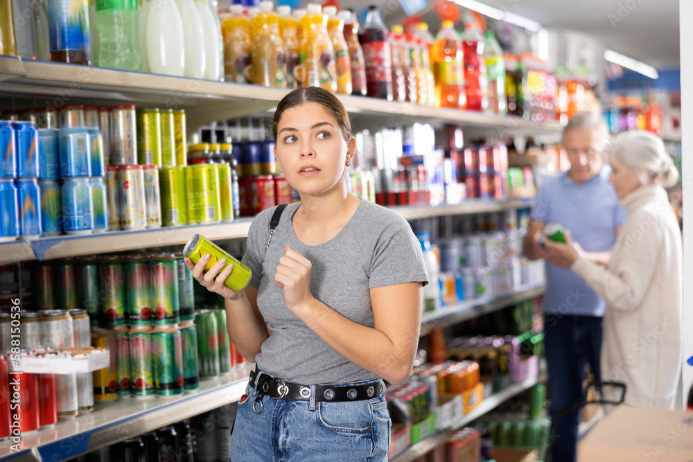 Young woman chooses carbonated drink in an aluminum can in the grocery section of a supermarket