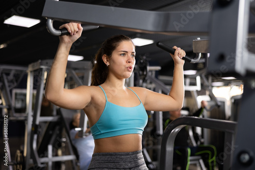 Young woman trains her arm muscles using a simulator in the gym