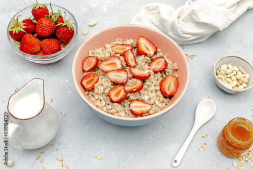 Oatmeal porridge with summer strawberries berries. Porridge oats in bowl with honey,milk,nuts. Healthy food breakfast,lifestyle,dieting, proper nutrition. Top view flat lay on gray table background