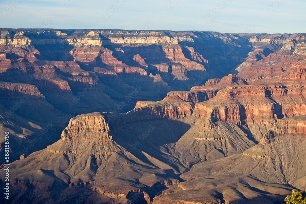 Bright desert sunlight shines down on the Grand Canyon, casting shadows on every crease and layer of the eroded canyon carved over many years by the Colorado River thousands of feet below