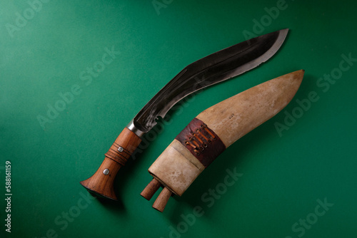 An ancient curved kukri knife and a wooden scabbard on a green background, a place for an inscription photo