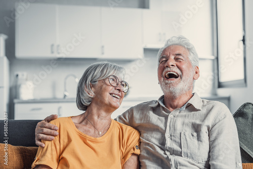 Happy mature husband and wife sit rest on couch at home hugging and cuddling, show care affection, smiling senior loving couple relax on sofa have fun, enjoy tender romantic family weekend together.