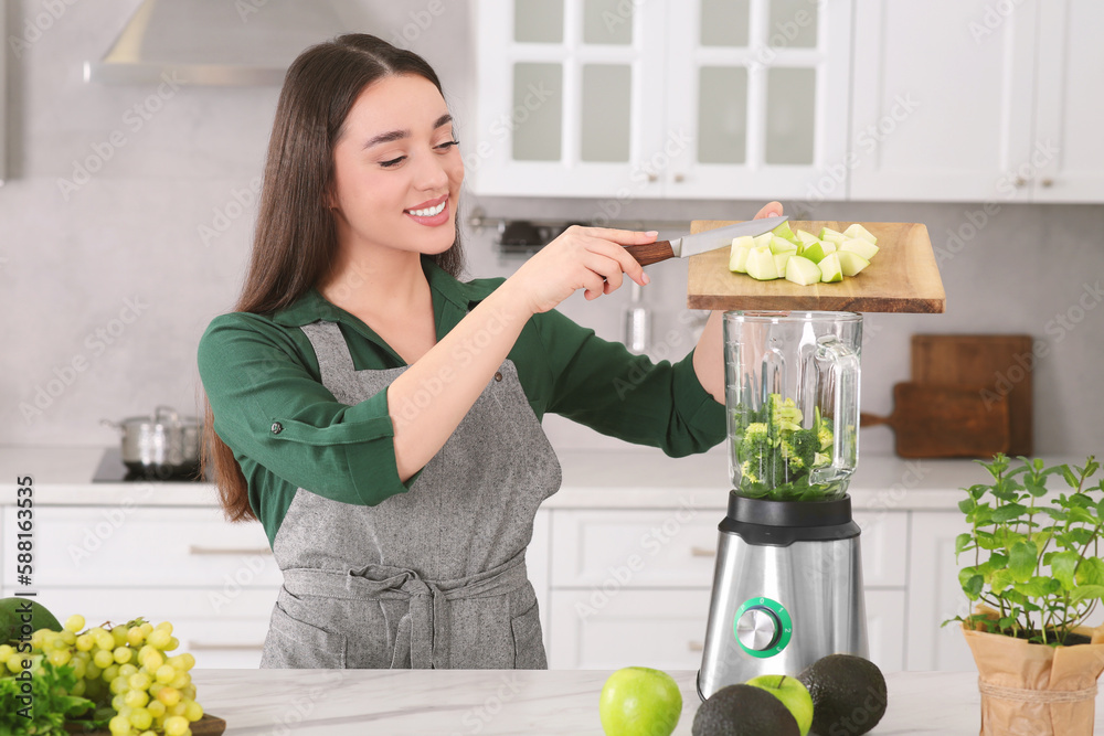 Woman adding apples into blender with ingredients for smoothie at white