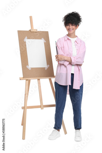 Young woman holding brush near easel against white background