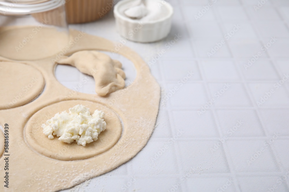 Process of making dumplings (varenyky) with cottage cheese. Raw dough and ingredients on white tiled table, closeup. Space for text