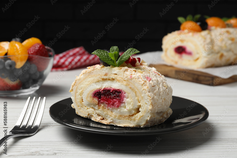 Slice of tasty meringue roll with jam and mint leaves on white wooden table, closeup Slice of tasty meringue roll with jam and mint leaves on white wooden table, closeup
