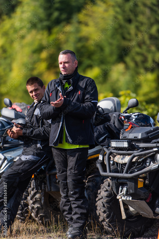Fototapeta premium A group of men on a social gathering are preparing to ride an ATV quad bike. People Ride together on a quad atv on muddy forest roads