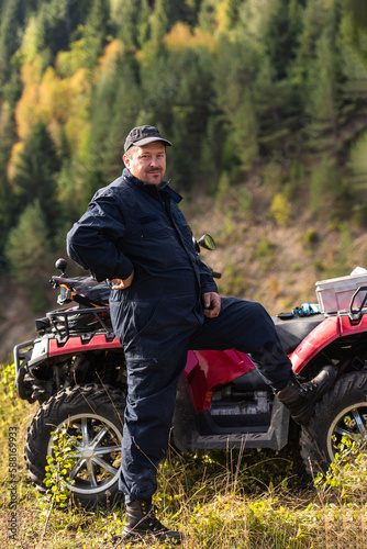 A man in a forest area posing next to a quad and preparing for ride