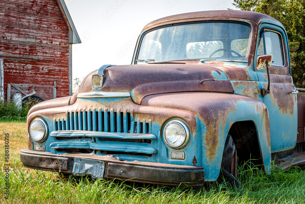 A vintage half ton pickup truck in front of a red barn on the Canadian prairies
