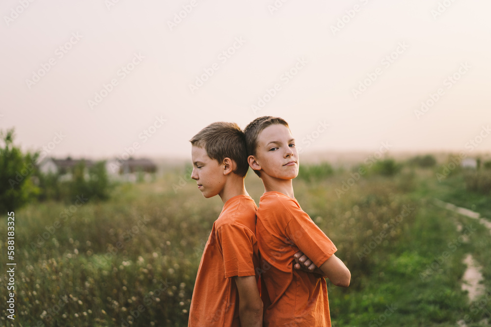 Funny twin brother boys in orange t-shirt playing outdoors on field at sunset. Happy children, lifestyle. Funny twin brother boys in orange t-shirt playing outdoors on field at sunset. Happy children, lifestyle.