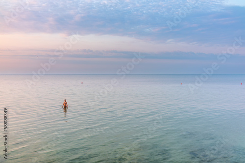 Young woman in brown swimwear going into the sea on the beach at sunrise
