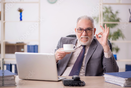 Old male employee drinking coffee in the office