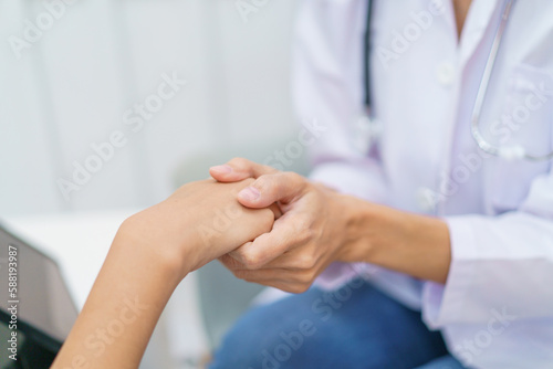 Female specialist or professional doctor giving a consulting to female patient in clinic. Doctor touching or holding on crisis patient's hand with empathy and care.