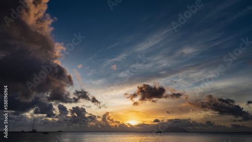 Fantastic tropical sunset over the ocean. The sun is low. The clouds are highlighted in scarlet and orange. Silhouettes of yachts and islands on the horizon. Seychelles. Mahe
