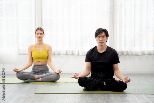 Young man and woman practicing yoga and meditating for relaxation and balance life on mat in the room at home, female and male sitting and training workout yoga exercise, health and sport concept.