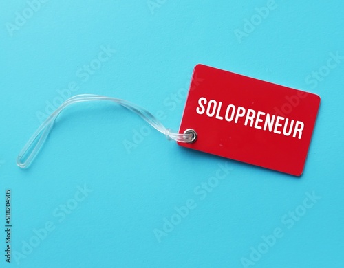 Red tag card on blue background with text written SOLOPRENEUR, person who sets up and runs business on their own, works independently and doesn't hire employees photo