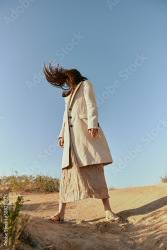 stylish woman in fashion style posing on the sand covering her face with her hair in motion