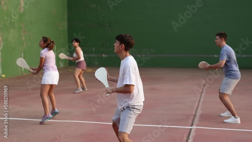 Group of sporty young people serving ball with special equipment, wooden paleta, during Basque pelota game outdoors. Boy playing pelota on outdoor fronton. photo