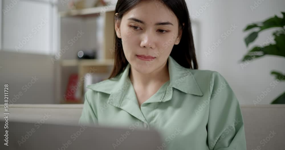 Handheld close up shot, Asian young woman sitting and drink beverage in mug, she smile with happy while use laptop computer in living room at home Handheld close up shot, Asian young woman sitting and drink beverage in mug, she smile with happy while use laptop computer in living room at home