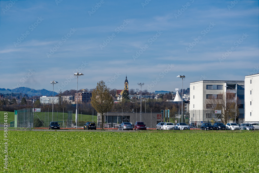 Emmenbrücke with church tower and scenic landscape, tennis courts, skyline and Swiss Alps in the background on a sunny spring day. Photo taken March 22nd, 2023, Emmen, Switzerland.