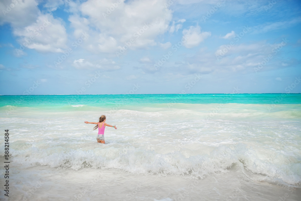 Holidays. Rest. Africa. Ocean. White sand. Beautiful baby on the ocean. Girl with long blond hair. Baby in a bathing suit Girl with a pigtail. The girl jumps on the waves. blue ocean