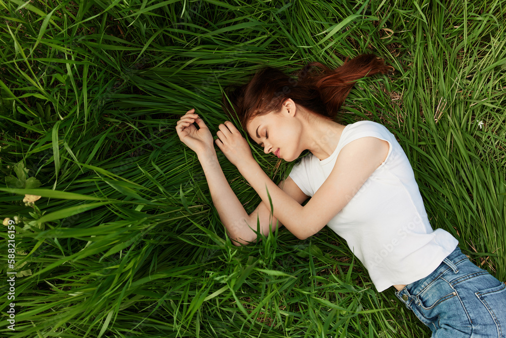 a red-haired woman lies in the tall grass in a white T-shirt and jeans a red-haired woman lies in the tall grass in a white T-shirt and jeans