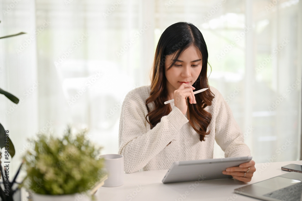 Serious and thoughtful young Asian woman using her tablet and laptop Serious and thoughtful young Asian woman using her tablet and laptop