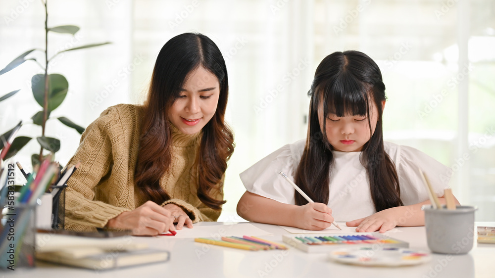 Attractive Asian sister helping her little sister to draw and paint with oil pastel color Attractive Asian sister helping her little sister to draw and paint with oil pastel color