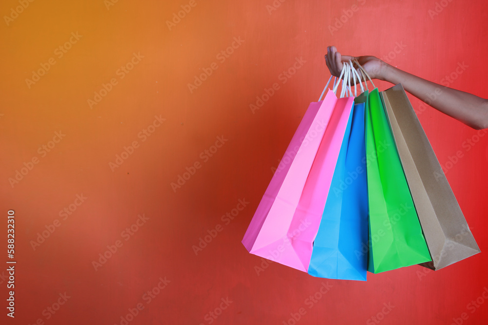 Colored paper bag in woman's hand on orange background