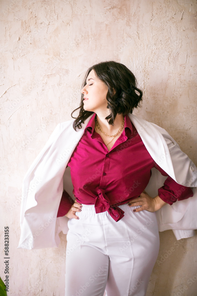 A young girl stylist with dark hair smiles in a trendy white jacket, a burgundy color shirt and light trousers in a light studio with green living plants in pots
A young girl stylist with dark hair smiles in a trendy white jacket, a burgundy color shirt and light trousers in a light studio with green living plants in pots