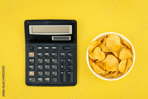 A plate of potato chips and a calculator on a yellow background, top view. photo