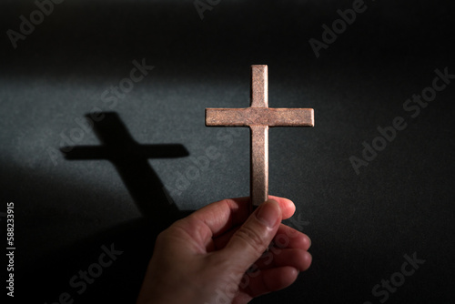 Hand holding wooden cross, with shadow on black background. Copy space.