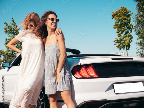Two young beautiful and smiling hipster female in convertible car. Sexy carefree women posing near cabriolet. Positive models riding and having fun in sunglasses outdoors. Taking selfie © halayalex