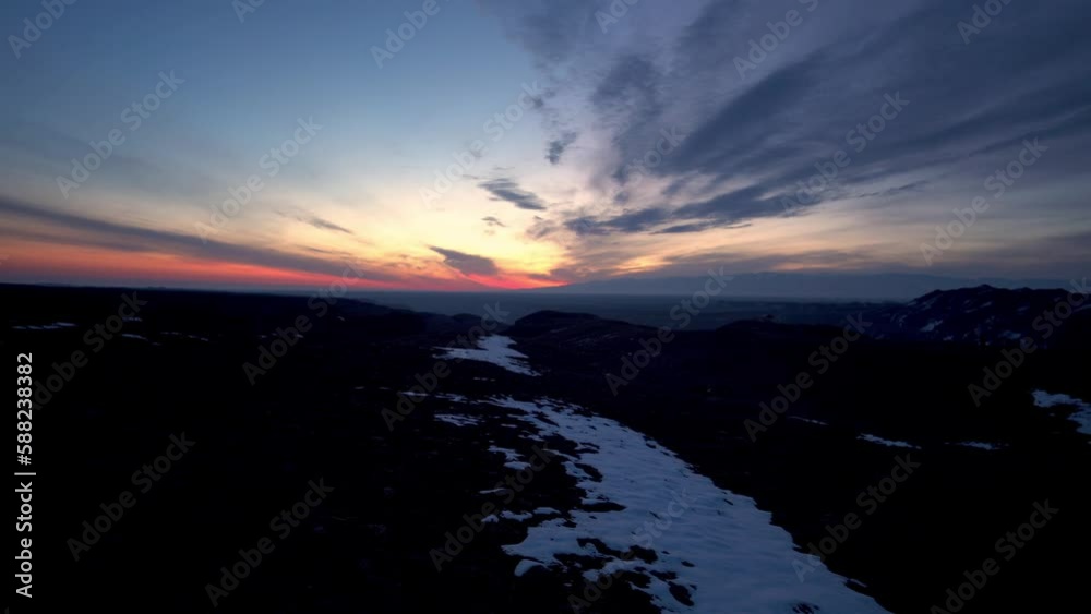 A red-orange sunrise with a view of the mountains and snow. Blue clouds hung in the sky. There is snow on the ground in places. Early morning. A haze is visible in the distance. A red-orange sunrise with a view of the mountains and snow. Blue clouds hung in the sky. There is snow on the ground in places. Early morning. A haze is visible in the distance.