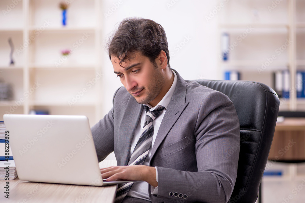 Young male employee unhappy with excessive work in the office Young male employee unhappy with excessive work in the office
