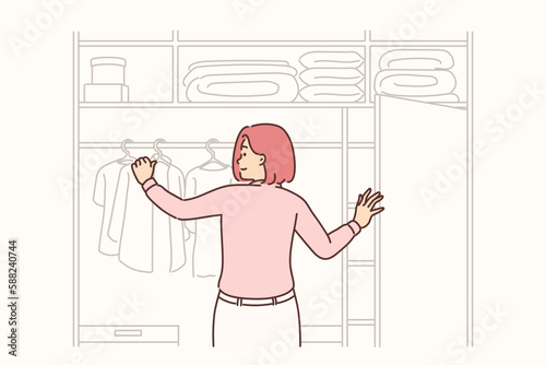 Woman stands with back to screen near large wardrobe closet choosing outfit for going to work 