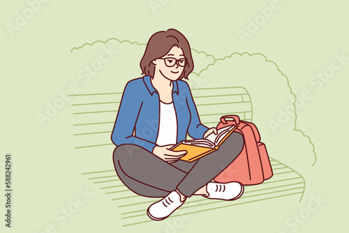 Teenage girl is reading book sitting on park bench enjoying good summer weather and intriguing plot of novel or fiction. Young woman spends leisure time outdoors doing self-education