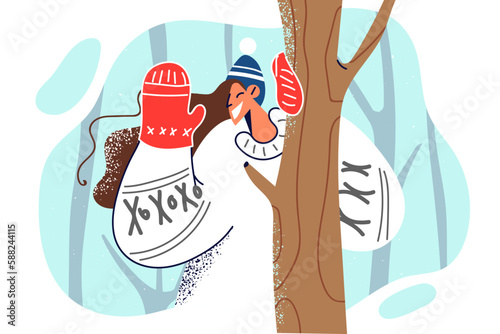 Woman in Scandinavian sweater waves hand standing in forest among trees during winter trip