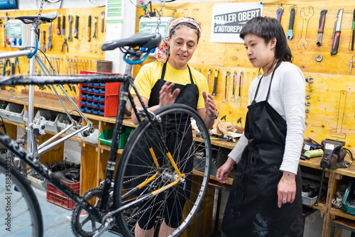 woman in her forties teaching a girl in her twenties how to fix a bike, girls in a bike repair shop, bike hung up for supervision and maintenance. photo