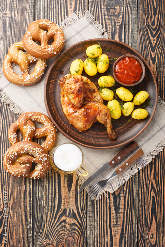 Bavarian roast chicken Hendl with boiled potatoes served with beer and pretzel closeup on the wooden table. Vertical top view from above