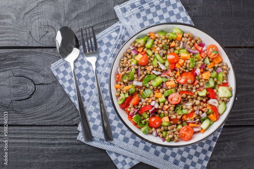 Vegetarian salad with boiled lentils, tomatoes, peppers, cucumbers, onions seasoned with olive oil close-up in a plate on a wooden table. Horizontal top view from above