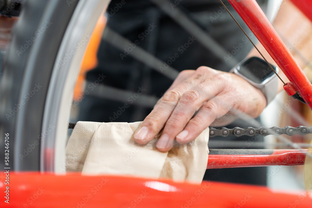 Detail of girl's hand cleaning bicycle in workshop, wrist with smart watch. Bike wheel and radios