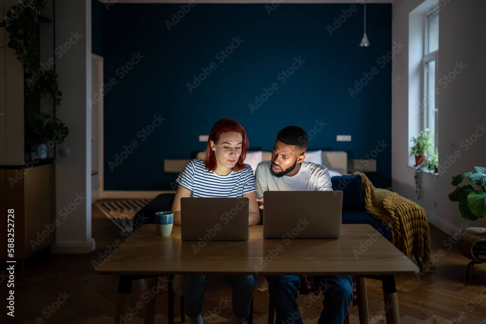 Young diverse entrepreneurial couple running small online business at home, multiracial family man and woman sitting at table working on laptops together in evening. Family entrepreneurship concept Young diverse entrepreneurial couple running small online business at home, multiracial family man and woman sitting at table working on laptops together in evening. Family entrepreneurship concept