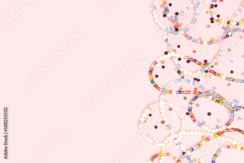 Necklaces and bracelets made from beads and pearls scattered on a pink background with copyspace.