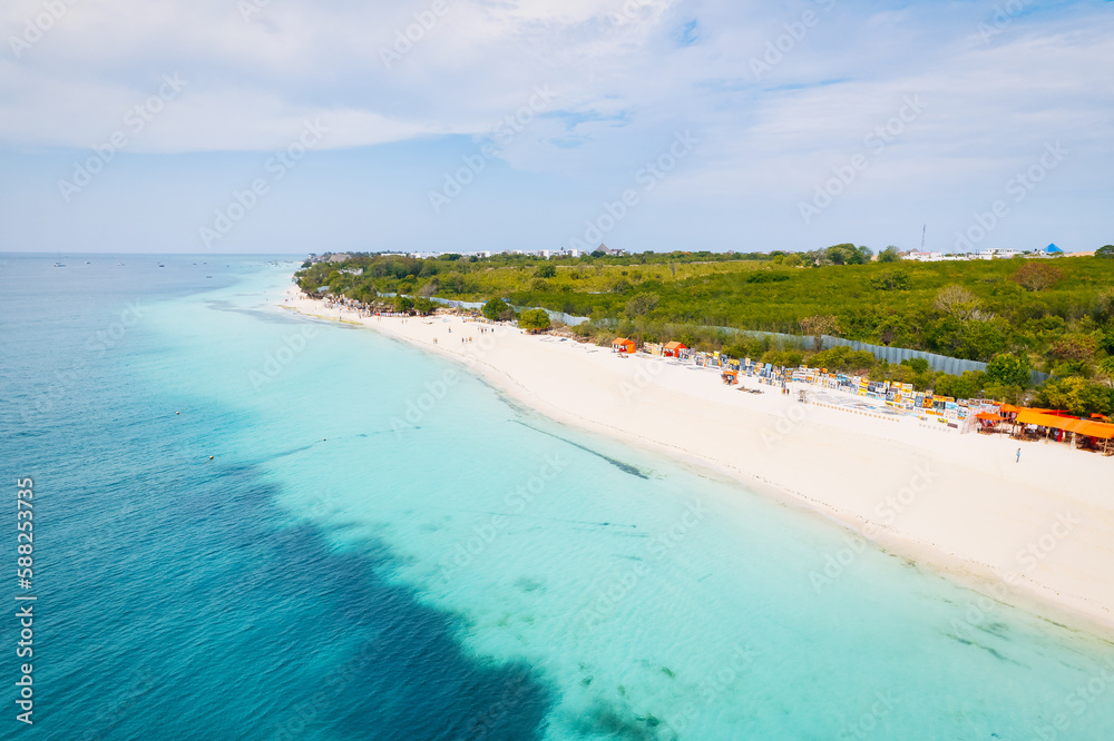 Fototapeta premium The aerial view of Zanzibar's beaches captures the essence of a tropical paradise with palm trees, umbrellas, white sand, and the sparkling blue waters of the Indian Ocean.